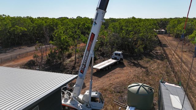 Xtreme Crane Hire crane lifting beside a new shed and water tank on a rural block