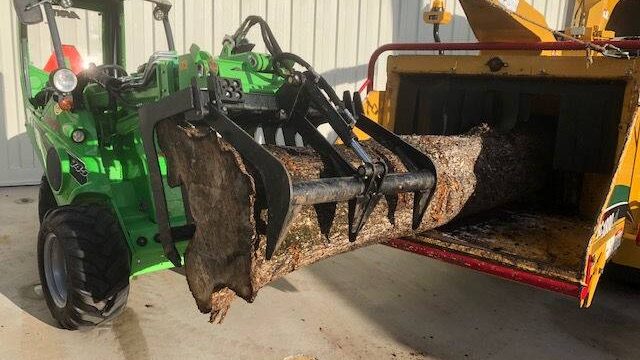 Xtreme Garden Care loader with grapple moving a large tree trunk into a chipper